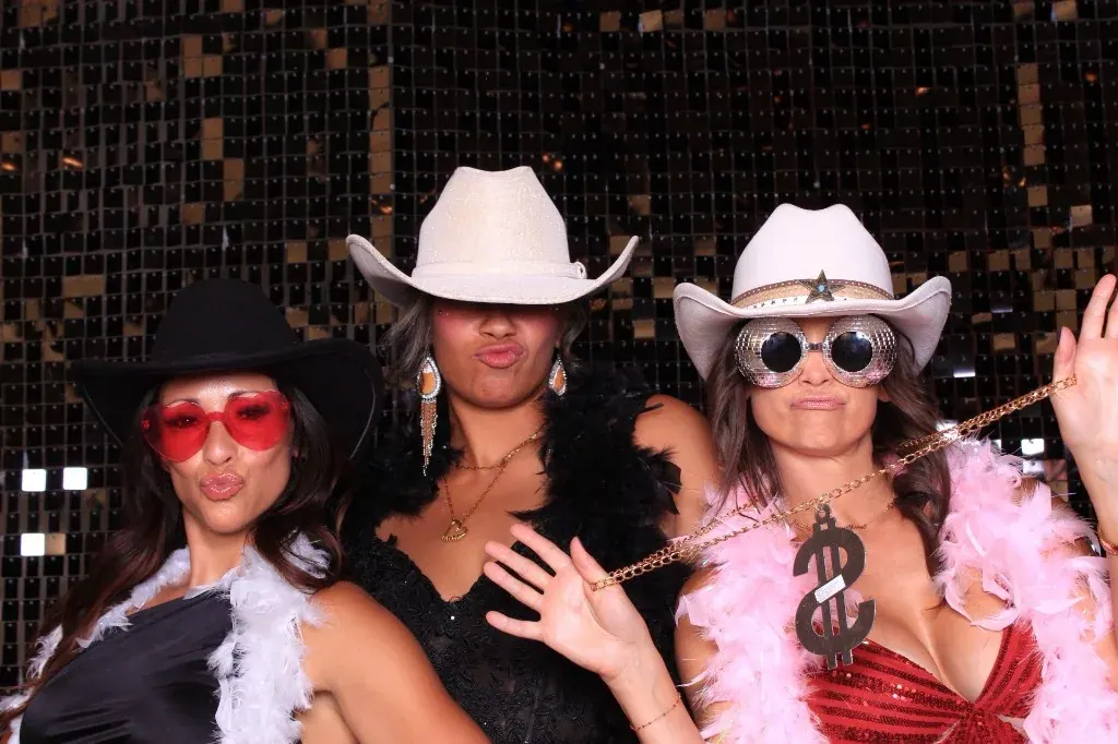 Three guests with feather boas, cowboy hats, and prop sunglasses
