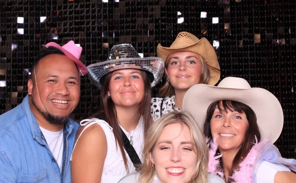 Corporate event guests in cowboy hats posing against a black sequin backdrop