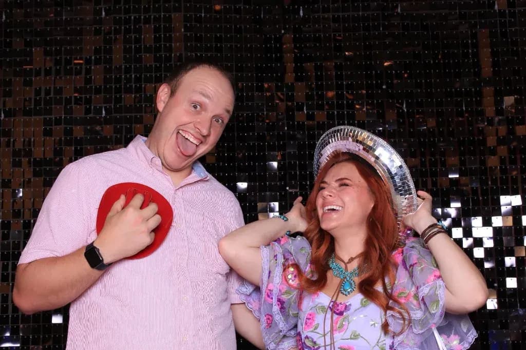 Couple laughing in the booth, one wearing a disco ball cowboy hat