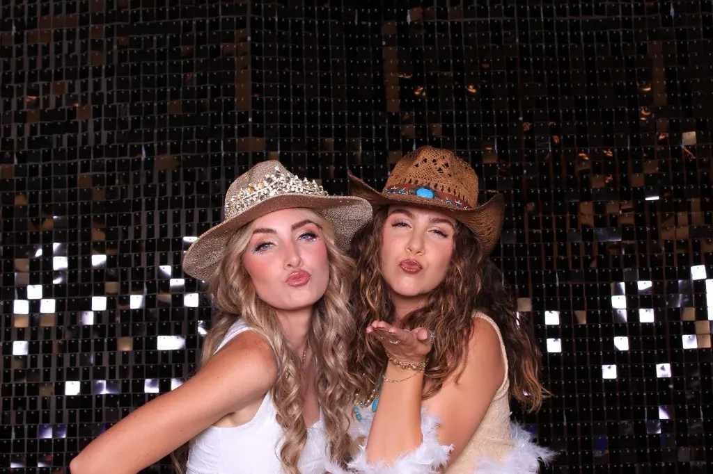 Two guests in glam cowboy hats blowing kisses at the booth
